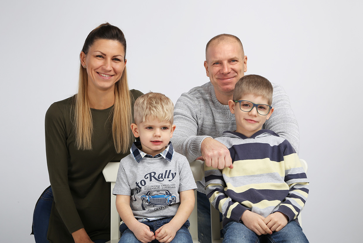 Natural Pharmaceuticals OmegaMarine Junior Mosolygós család képe, két felnőtt és két gyerek egymás mellett, egyszínű háttér előtt.