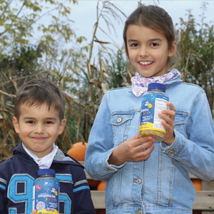Natural Pharmaceuticals OmegaMarine Junior Mosolygó gyerekek tartanak vitaminos táplálékkiegészítőket kerti környezetben.