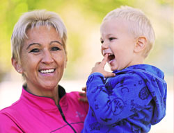 Natural Pharmaceuticals OmegaMarine Junior Mosolygó nagymama tartja és nézi játékosan a kisfiút napsütéses háttér előtt.
